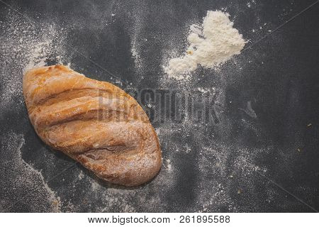 A Loaf Of White Bread On Dark Kraft Paper, Powdered With Flour.