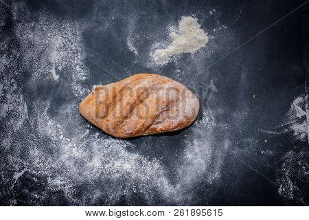 A Loaf Of White Bread On Dark Kraft Paper, Powdered With Flour.