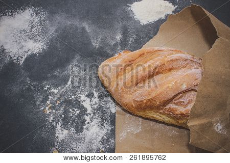 A Loaf Of White Bread On Brown Craft Paper, Powdered With Flour On A Dark Table Background.