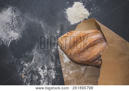 A Loaf Of White Bread On Brown Craft Paper, Powdered With Flour On A Dark Table Background.