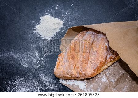 A Loaf Of White Bread On Brown Craft Paper, Powdered With Flour On A Dark Table Background.