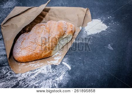 A Loaf Of White Bread On Brown Craft Paper, Powdered With Flour On A Dark Table Background.