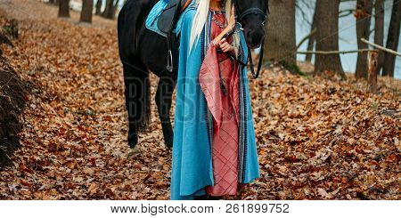 A Girl In A Pink Vintage Dress, With Long Hair, A Blonde In A Blue, Old-fashioned Cape, Stands Besid