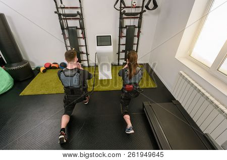 Back View Of Man And Woman In Electro Muscular Stimulation Suits Squatting
