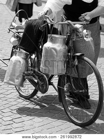 Elderly Woman Carrying Milk Cans With An Old Rusty Bicycle  And Black And White Effect