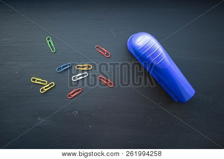 A Stepler And Colored Clips On Black Background