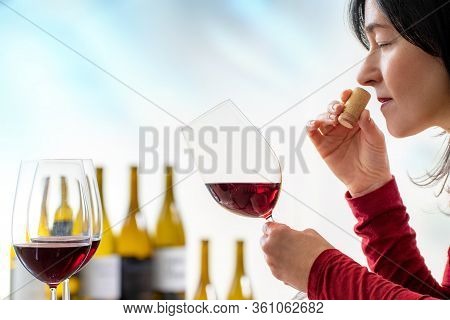 Close Up Of Female Enologist Smelling Wine Cork At Tasting. Woman Holding Red Wine Glass With Out Of