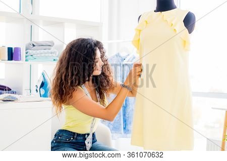 Lovely tailor girl putting pin in dress on mannequin