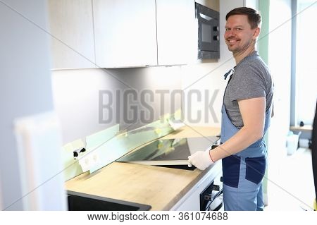 Portrait Of Cheerful Handyman Setting Cookstove On Kitchen. Professional Service Worker In Uniform H