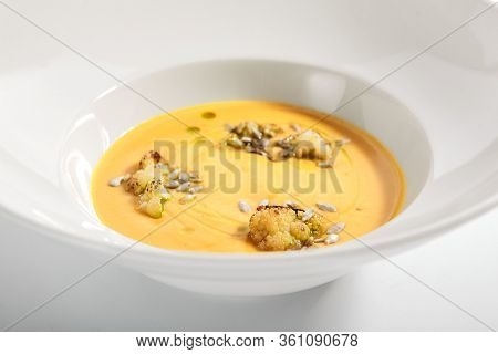 Pumpkin soup in white bowl. Served main course close up. Vegetable cream soup decorated with seeds. Restaurant food portion, main course. Vegetarian supper. Dinner, gourmet meal in plate