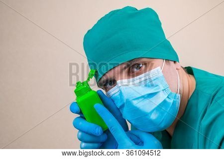 Doctor In Green Suit And Blue Mask Gloves With Green Antiseptic Bottle In Hand On Yellow Background.