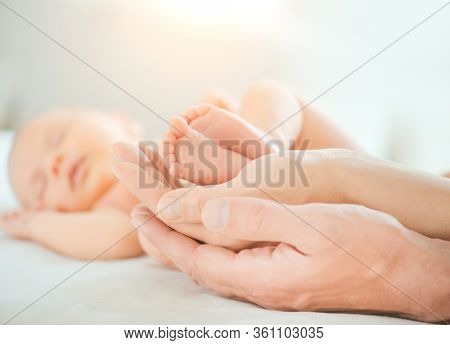 Baby feet in mother and father hands. Tiny Newborn Baby's feet on hands closeup. Mom, Dad and Child together. Healthy and Happy Family concept. Parents. Beautiful photo of Parenthood, adoption 