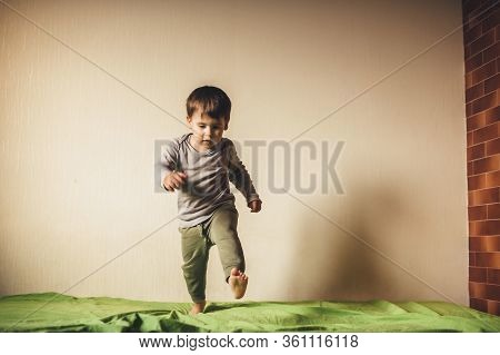 Caucasian Boy Jumping On The Green Sofa And Playing In The Bedroom