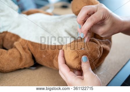 Female Hand With Blue Nail Polish Sewing A Ripped And Dirty Teddy Bear