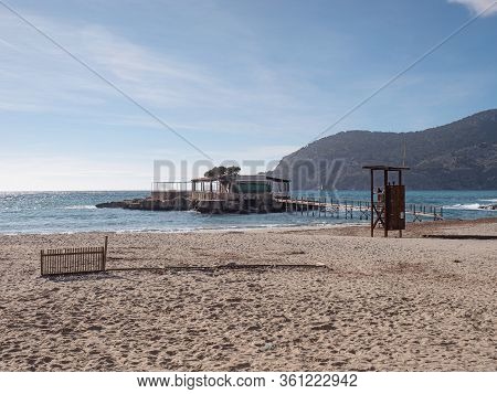 Travelers Walking On Beach In Peguera Resort, Majorca. Island With Restaurant And Bar On Small Islan