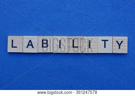 The Word Lability From Gray Small Wooden Letters With Black Font Lies On A Dark Blue Table