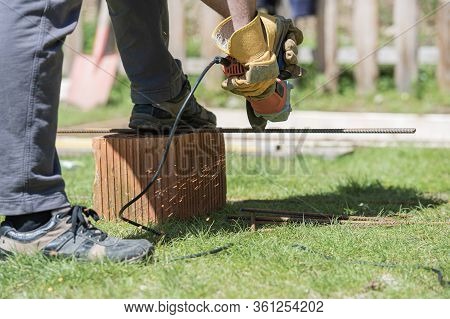 Low Angle View Of A Man Wearing Protective Gloves Cutting Steel Rod With A Circular Saw, Working On 