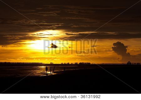 Homme marchant le long de la plage au coucher du soleil