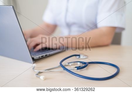 Unrecognizable Female Doctor In Uniform Uses A Laptop. Faceless Medical Worker Writes A Report On Th