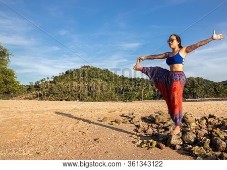 Asian Thai Woman Practicing Yoga At Evening In Mae Haad Beach, Koh Phangan Island, Thailand.