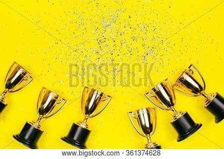 Golden Winner Cups With Silver Sparkles On A Yellow Background With Copy Space. Festive Concept. Fla