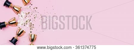 Golden Winner Cups With Sparkles On A Pink Background With Copy Space. Festive Concept. Flat Lay Sty
