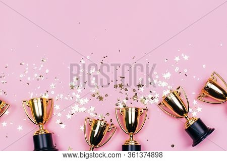 Golden Winner Cups With Sparkles On A Pink Background With Copy Space. Festive Concept. Flat Lay Sty