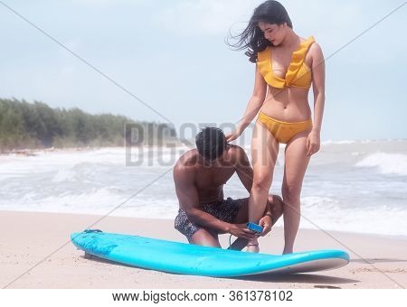 Young Handsome Man Teaching Basic Of Serfing For Beautiful Woman Wearing Swimsuit,on The Beach