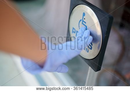 Hand Wearing Blue Glove Pressing Handicapped  Button To Open Door