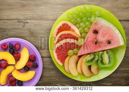 Sliced Fruit On A Borwn Wooden Background. Sliced Fruit On A Light Green Plate Wit Fruits On A Purpl