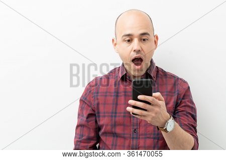 Caucasina Bald Man In His 30s Looking Shocked And Surprised While Looking At His Smartphone In A Stu