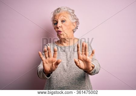 Senior beautiful woman wearing casual t-shirt standing over isolated pink background Moving away hands palms showing refusal and denial with afraid and disgusting expression. Stop and forbidden.