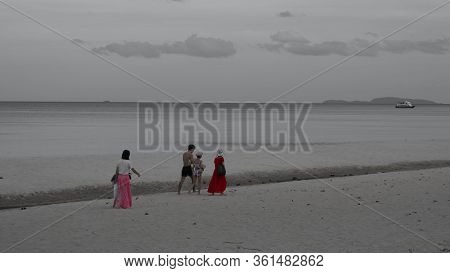 Women In Sarongs With Man, Girl And Child Walking Along Beach With Boat In The Background