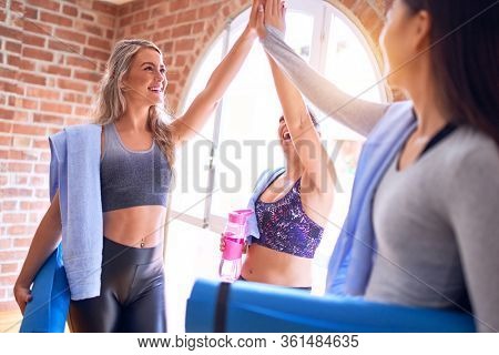 Young beautiful group of sportswomen smiling happy. Standing shaking hands with smile on face after class of yoga at gym