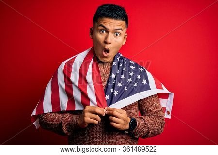 Young handsome latin patriotic man wearing united states of america falg scared in shock with a surprise face, afraid and excited with fear expression
