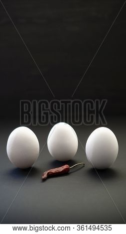 Elegant Easter Celebration. Three White Eggs Stand Upright And Red Chili Peppers On A Dark Surface.