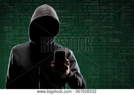 Anonymous Computer Hacker With A Smartphone Over Abstract Digital Background. Obscured Dark Face In 