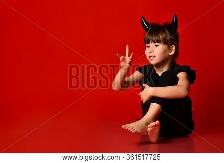 Little Brunette With Devilish Horns, In A Black Blouse And Leggings, Barefoot. She Looks At Her Rais