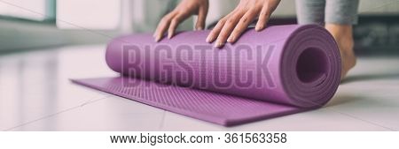 Yoga at home woman rolling pink exercise mat in living room starting warm up meditation zen well being wellness banner panoramic apartment living room lifestyle.