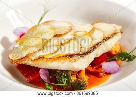 Fried flounder fillet on baked potato slices. Served luxury cuisine. Fish with tomato and olives ragout in white plate isolated. Restaurant high menu food portion. Delicious supper, main course