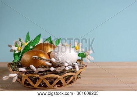 Easter Eggs In Basket Filled With Straw And Yellow Flowers And Willow. Preparation For Holiday. East