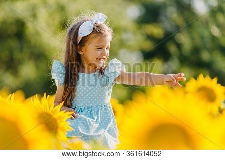Little Cheerful Girl In A Field Of Yellow Sunflowers. Child And Sunflower, Summer, Nature And Fun. S
