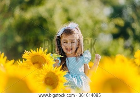 Little Cheerful Girl In A Field Of Yellow Sunflowers. Child And Sunflower, Summer, Nature And Fun. S