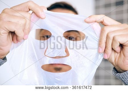 closeup of a caucasian man about to apply a bio-cellulose sheet mask to his own face
