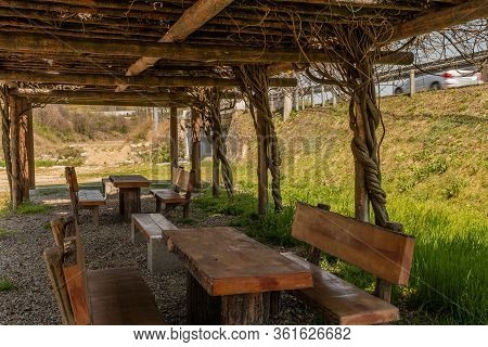 Shelter Of Wood And Vines Over Picnic Tables And Benches At Local Public Park.
