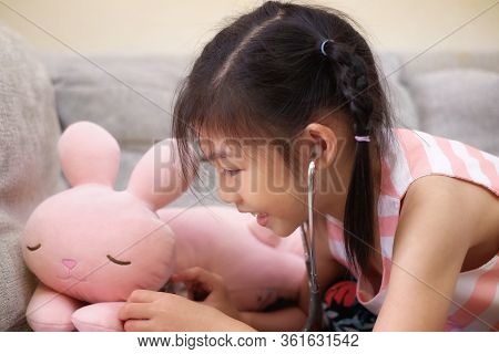 An Asian Girl Playing Doctor With A Stethoscope On Her Pink Rabbit, Smiling.