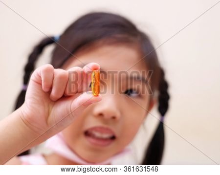 A Girl Holding A Fish Oil Capsule, Getting Ready To Take Her Medicine.