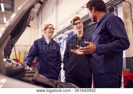 Male Tutor With Students Looking At Car Engine On Auto Mechanic Apprenticeship Course At College