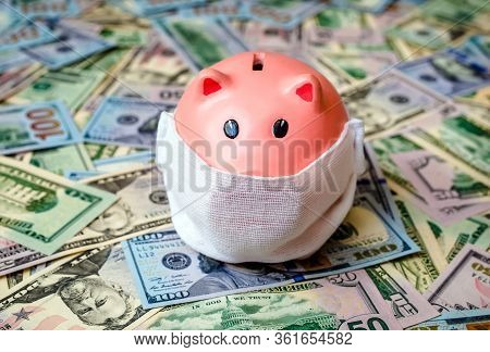 Piggy Bank In A Mask On A Background Of American Currency.the Concept Of Coronavrius Epidemic