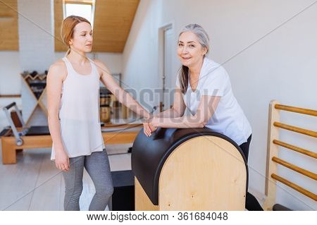 Young Professional Instructor Helping An Elderly Woman Cant Workout Independently Doing Stretching B